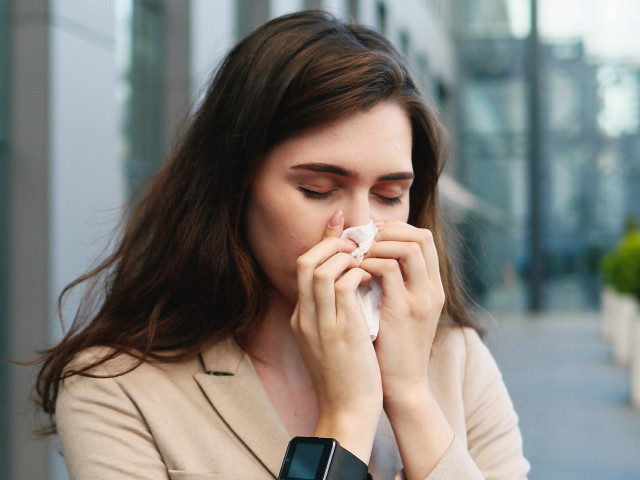 Młoda kobieta z alergią stoi w mieście i dmucha nos